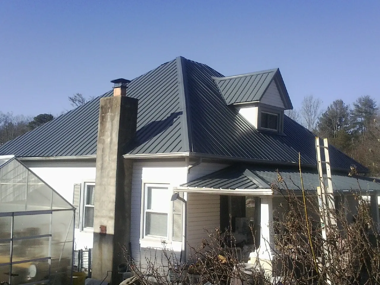 Dark blue standing seam metal roof on a white farmhouse with dormer — Slate & Tile Roof Repair by Roofing Brothers in Decherd