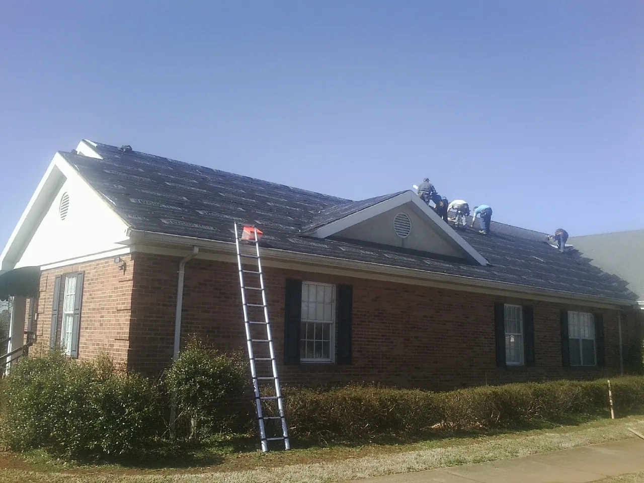 Crew tearing shingles off a brick ranch roof with a ladder set — Metal Roof Repair work by our crew in Decherd