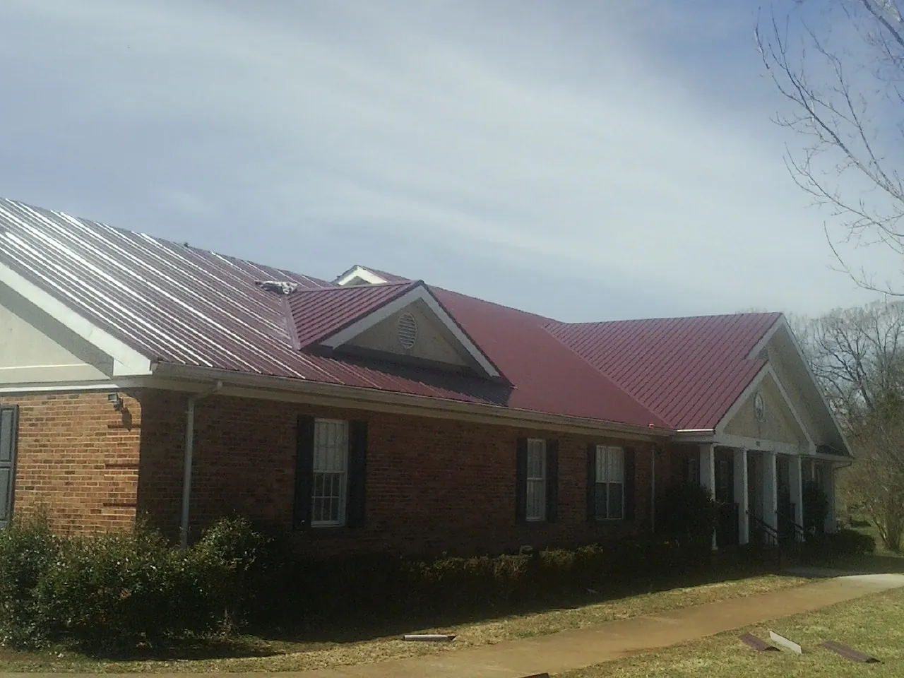 Red metal roof with gabled entries on a long brick building, from a Hail Damage Roof Repair job in Decherd