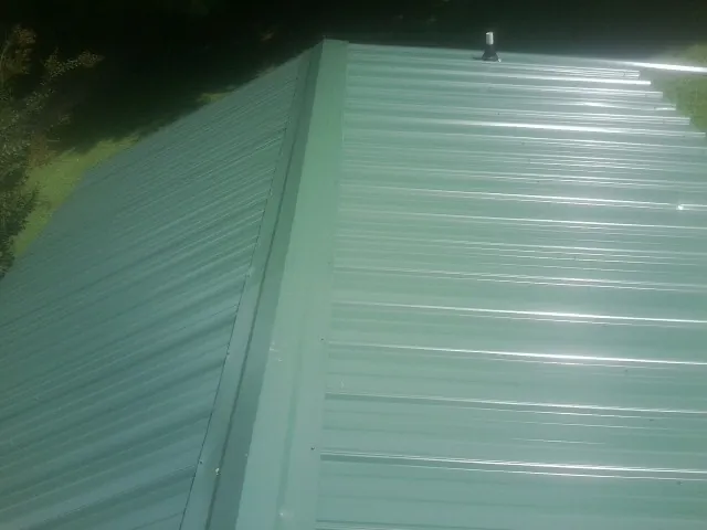 New green metal panels meeting at the ridge of a roof — Flat Roof Repair work by our crew in Decherd