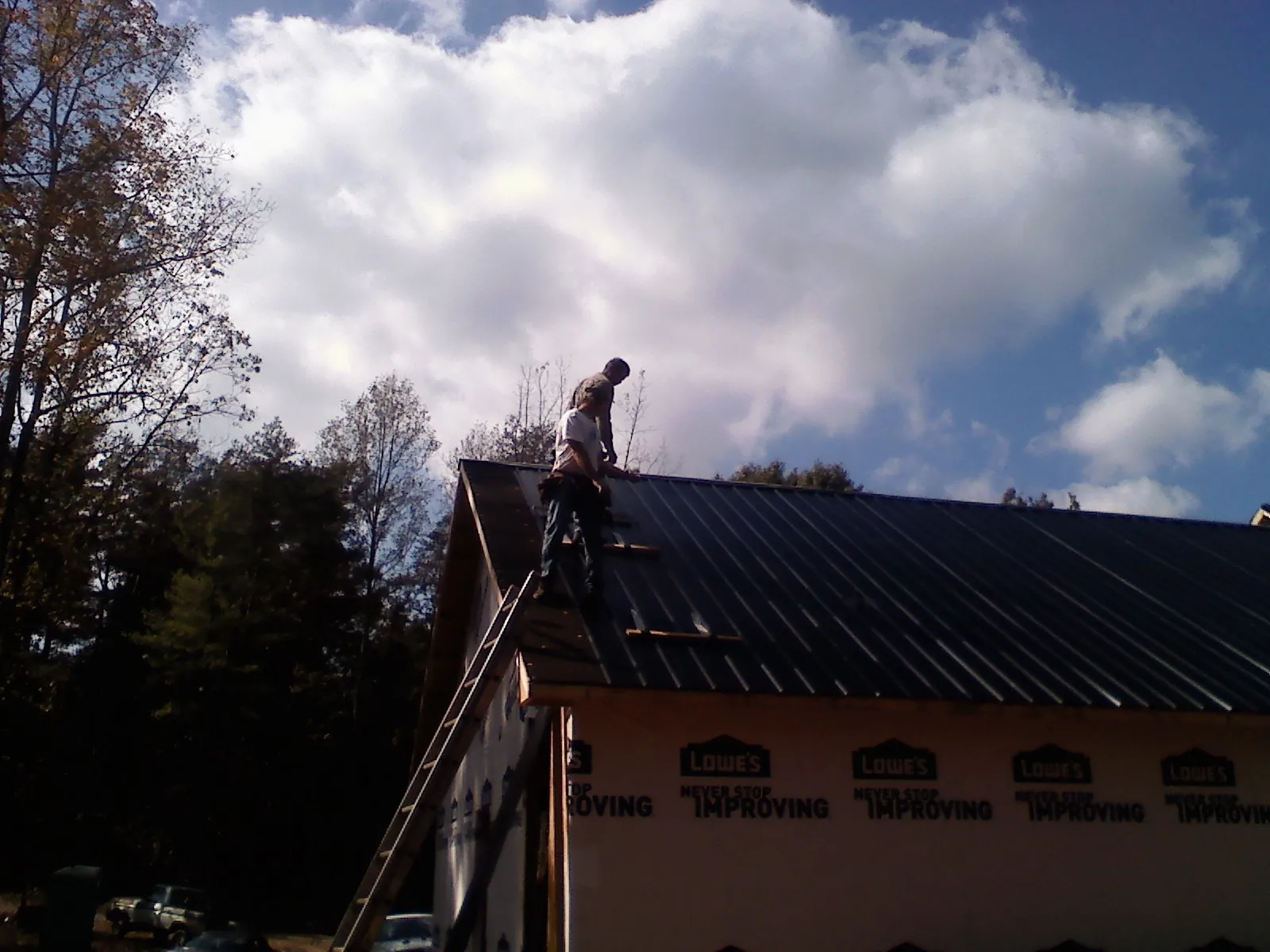 Roofer fastening dark metal panels high against a cloudy sky, from a Roof Inspection job in Decherd