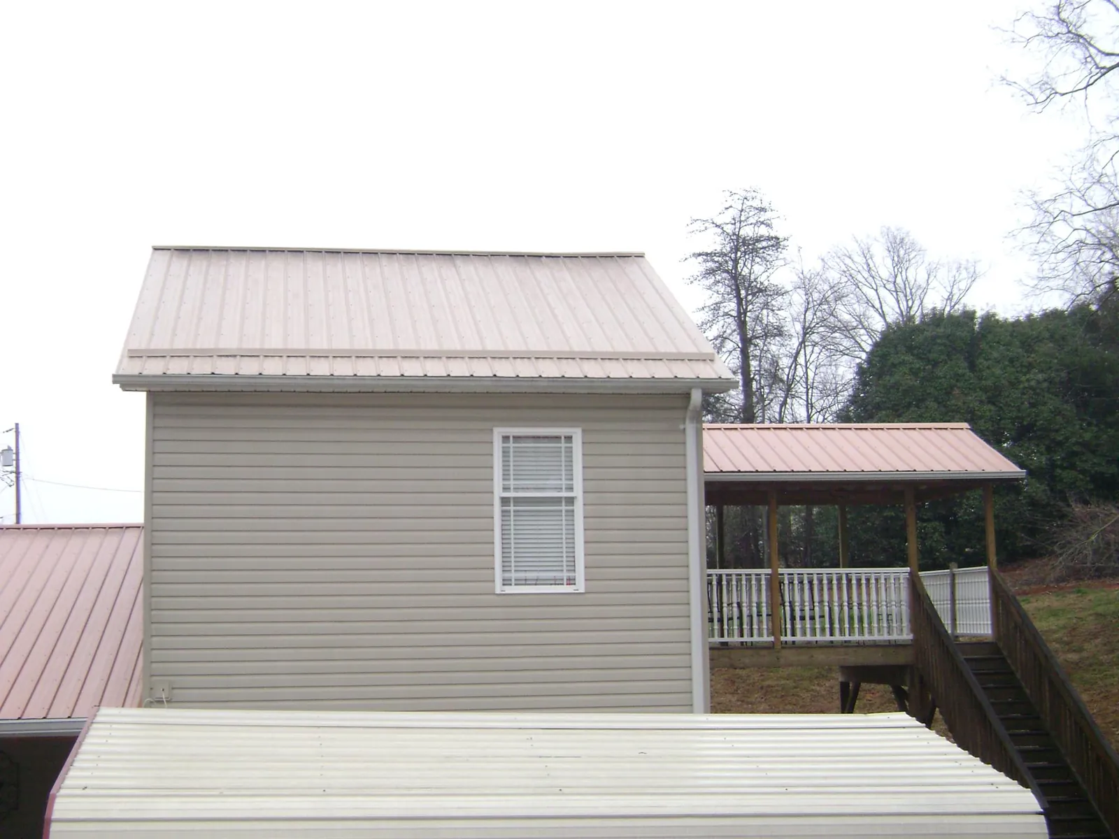 Tan metal roofs on a two story addition and attached porch, from a Roof Replacement job in Decherd